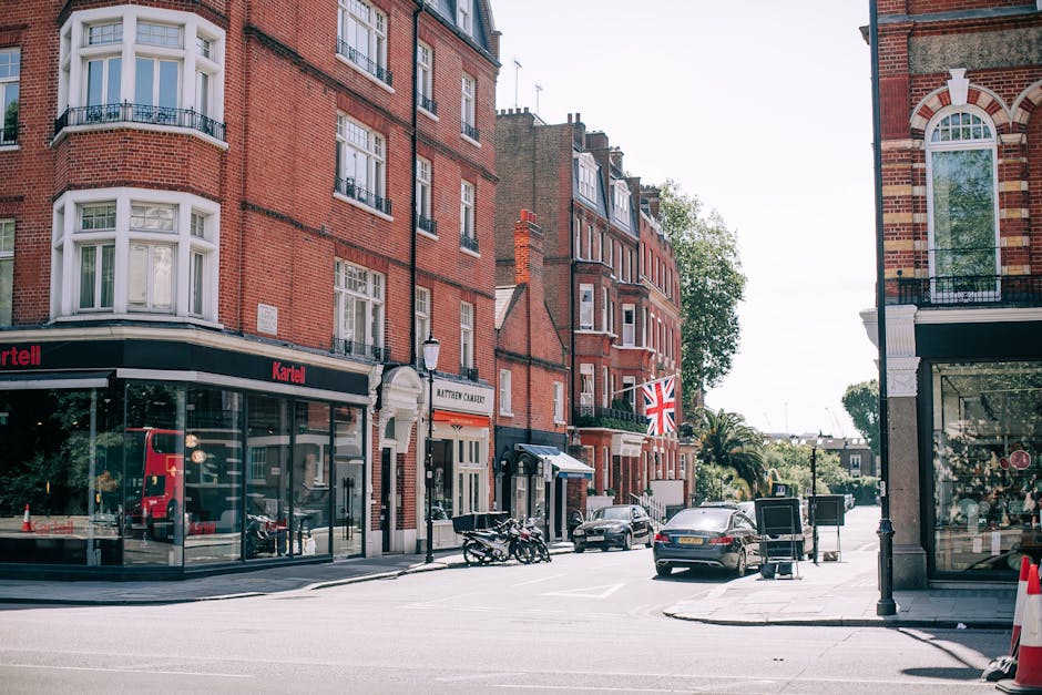 A red double-decker bus with a digital route display indicating route 453 to Marylebone is parked on a wet urban street near the historic buildings of Westminster, London, with black bollards and a metal railing along the sidewalk. The background features Gothic-style architecture of the Palace of Westminster, with spires and detailed stonework, under a cloudy sky, and flags flying along the nearby street. The scene captures a typical day in Marylebone, showcasing city transport and historic surroundings, with clean, wet surfaces reflecting the bus and nearby structures. For professional cleaning and maintenance of similar urban environments, visit Cleaners Marylebone at cleaners-marylebone.com.
