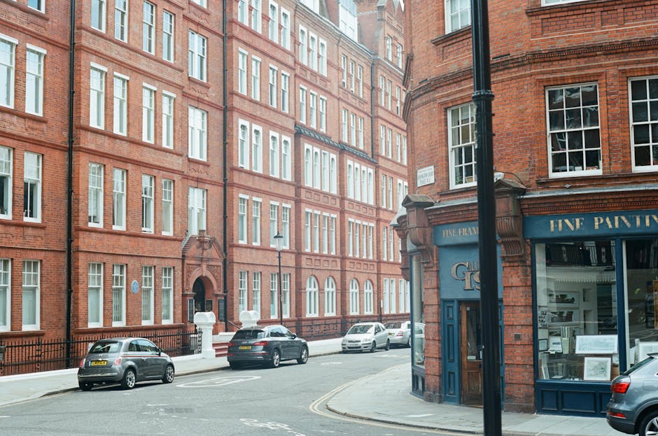 Street view of red brick residential buildings in Marylebone, London, with large windows and decorative architectural details. The scene includes parked cars along the curb and a corner shop with a blue facade labeled 'Fine Paints,' featuring display windows and a door, illuminated by natural daylight. The overall environment appears clean and well-maintained, reflecting a typical urban streetscape near a residential area. Cleaners Marylebone provides domestic and commercial surface cleaning and deep cleaning services, ensuring hygiene and shine in similar environments.