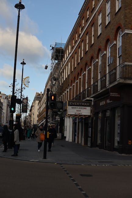 Exterior view of a multi-storey building featuring traditional brickwork and large windows, with two black-framed signs hanging from the facade displaying the name 'The Marylebone' and related details